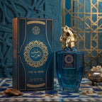 A bottle of Taif Al Arab Eau de Parfum with a metallic horse-shaped cap stands beside its matching blue and gold box on a patterned surface, with a decorative blue and gold background.